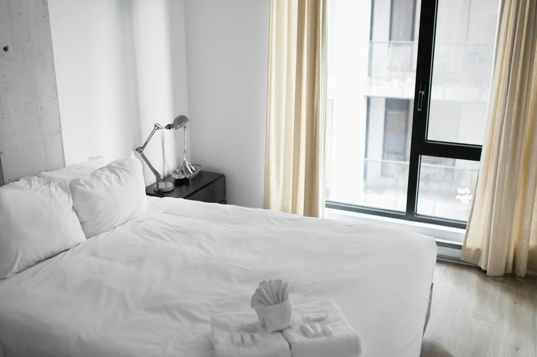 Helles Hotelzimmer mit weißem Doppelbett, gefalteten Handtüchern und einem großen Fenster.
